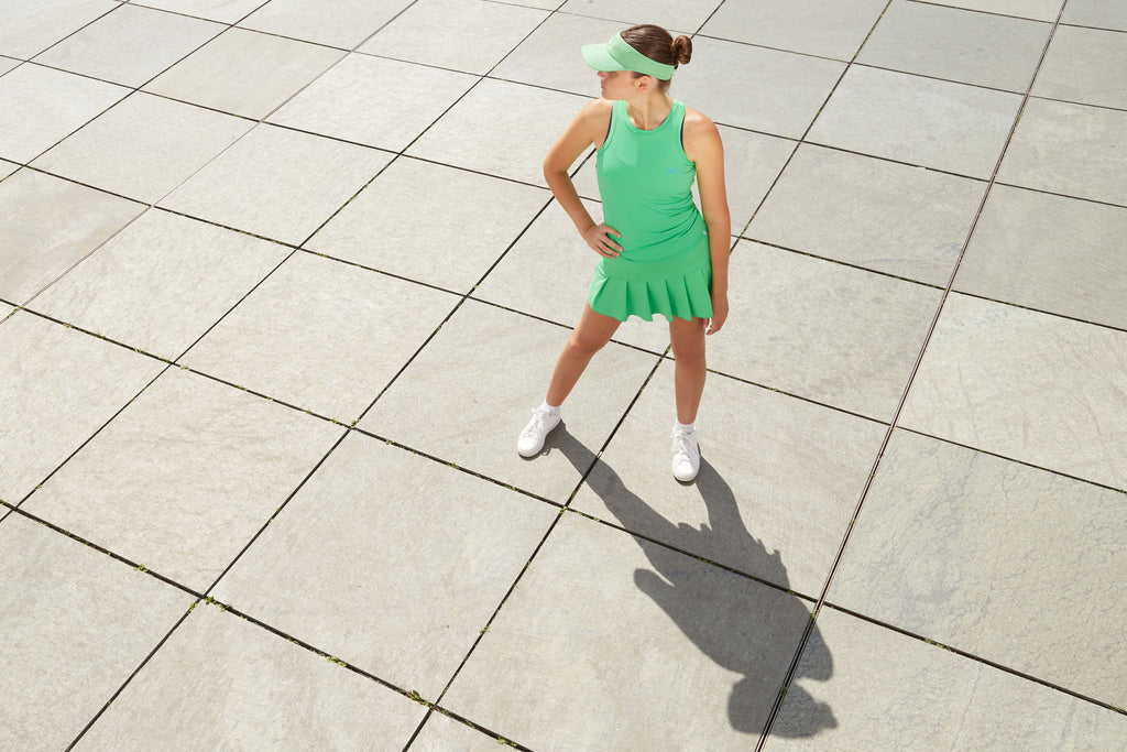 Damen mit grüner Tenniskleidung bestehend aus Faltenrock, Top und Sun Visor